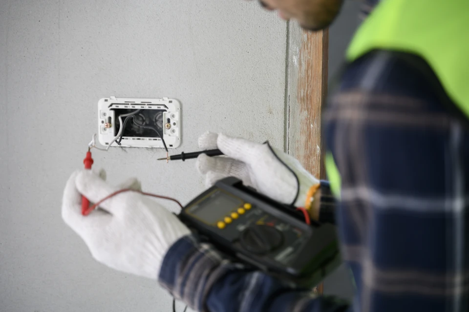 Photo d'un électricien professionnel en gilet de chantier réfléchissant, intervenant rapidement dans un intérieur résidentiel pour répondre à une urgence électrique. L'électricien doit être photographié en action, examinant un tableau électrique ouvert ou travaillant sur une installation défaillante, montrant mobilité, réactivité et professionnalisme. L'image doit transmettre un sentiment d'urgence et d'efficacité, avec du matériel électrique visible et un environnement intérieur réaliste.