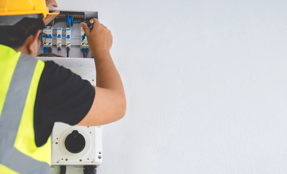 Électricien professionnel en tenue de travail (chemise et pantalon), mesurant ou diagnostiquant une installation électrique avec un multimètre numérique sur un tableau électrique résidentiel ou commercial. L'électricien doit être en train de vérifier les connexions ou les circuits avec concentration et professionnalisme. Photo réaliste de qualité professionnelle, prise en intérieur d'un habitat ou local commercial, montrant clairement le travail technique de diagnostic et suivi électrique.
